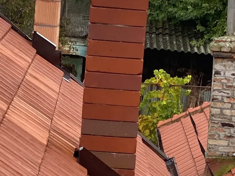 Coș de cărămidă pe un acoperiș din țiglă ceramică, cu șorțul de tablă la bază