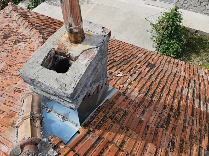 Coș de fum pe un acoperiș vechi din țiglă ceramică, cu tubul de inox și tabla de la bază