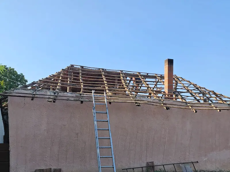 Casă cu acoperișul desfăcut până la căpriori și o scară sprijinită de perete