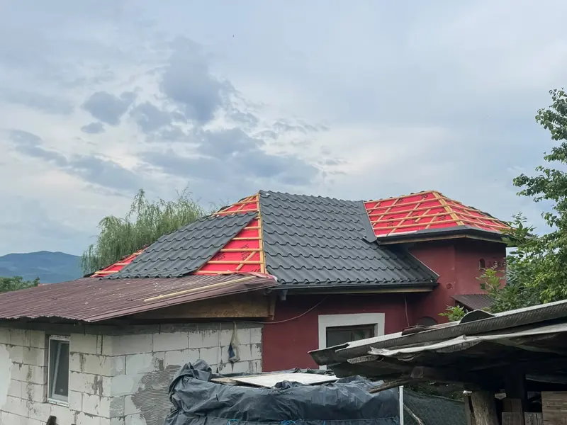 Casă roșie cu acoperișul în lucru: o parte cu țiglă veche, o parte acoperită deja cu țiglă metalică gri