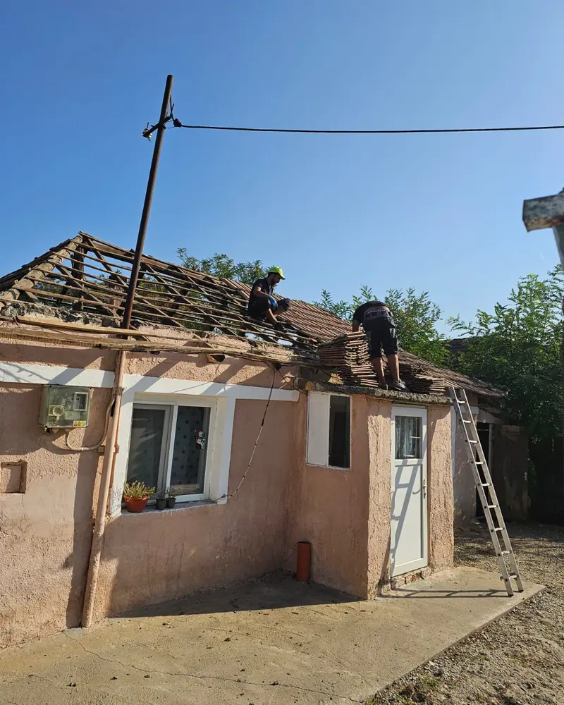 Casă roz cu acoperișul desfăcut și doi oameni din echipă pe șarpantă