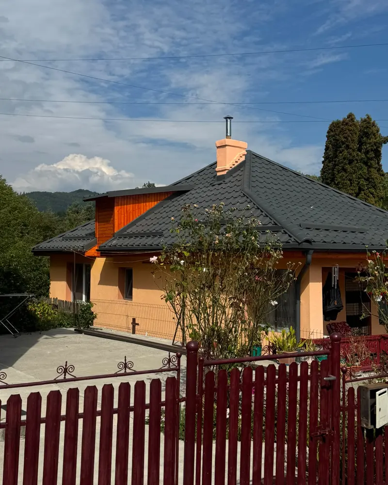 Casă portocalie cu acoperiș din țiglă metalică închisă la culoare, cu un gard roșu în față