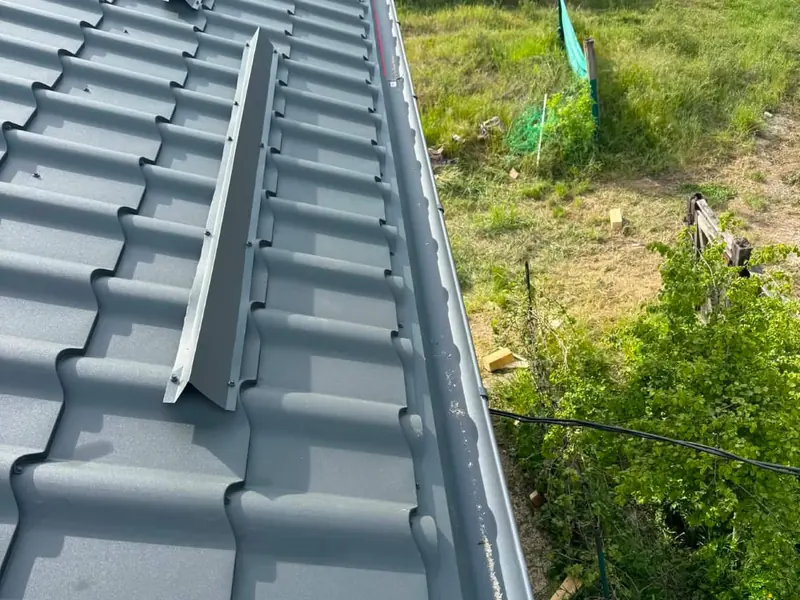 Marginea unui acoperiș din țiglă metalică gri, cu bordura laterală și parazăpezile